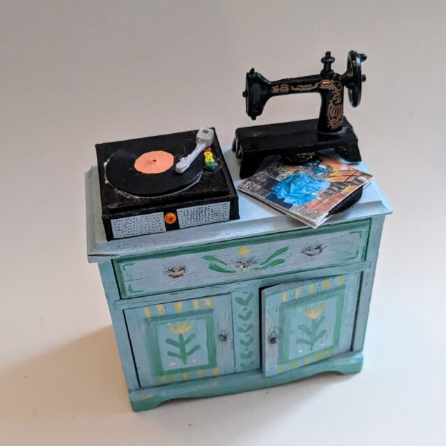 🏡 This cute little cabinet was just a kit that my mom found at the thrift store ages ago, (I don't think it's even technically to scale), but I gave it a paint job and it fits very well I think. 
This record player is something that my brother made me for my birthday! The arm moves and it goes perfectly with my mini Hozier album that matches my real-life vinyl! (The sewing machine was bought for me❤)

#dollhouse #dollhousemakeover #miniatures #dollhousedecor #upcycle #handmadecrafts #dıy #montanaartist