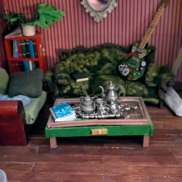 🏡 Another early piece for my dollhouse! I would love to someday make one of the curio cabinet coffee tables for real, but for now I made a mini one! 
This is mostly made from toothpicks and little bits of wood. The lid is a clear bit of plastic I found, and the hinges are just paper. Set on top are a book, a pencil made from a toothpick end, a tube of paint (bought), and a tea set that I bought and added a few bead mugs to.

 #dollhouse #dollhousemakeover #miniatures #dollhousedecor #upcycle #handmadecrafts #dıy #montanaartist