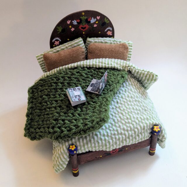 🏠The Dollhouse Bed!! One of the first things that I made for my dollhouse! I spent a lot of time trying to make it look like the comfiest one in existence. I specifically wanted to source a fabric for the bed spread with stripes to scale. (I ended up cutting up a skirt from the thrift.) 
The bed frame is made from some craft wood that I stained and painted and the pattern was from this awesome dollhouse book we've had as long as I can remember. I knitted the throw and had my brother 3D print the laptop adorning the bed.
Also, I thought this would be a good place to showcase the little button and bead picture frames that are so perfect for the space!

 #dollhouse #dollhousedecor #dollhousemakeover #miniatures #upcycled #handmadecrafts #dıy #sewingproject #montanaartist